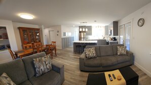 Una sala de estar moderna con un sofá gris, una mesa de comedor y una cocina al fondo.