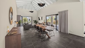 Un comedor amplio con una gran mesa de madera y sillas modernas, un techo con vigas a la vista y vistas al exterior a través de ventanas grandes.