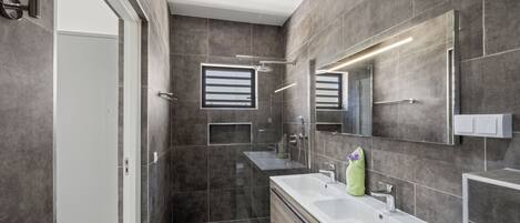 A modern bathroom with two sinks, a mirror, and a shower.