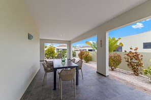 Eine moderne Terrasse mit Esstisch und Stühlen, umgeben von einem Garten mit verschiedenen Pflanzen und Blick auf benachbarte Häuser.