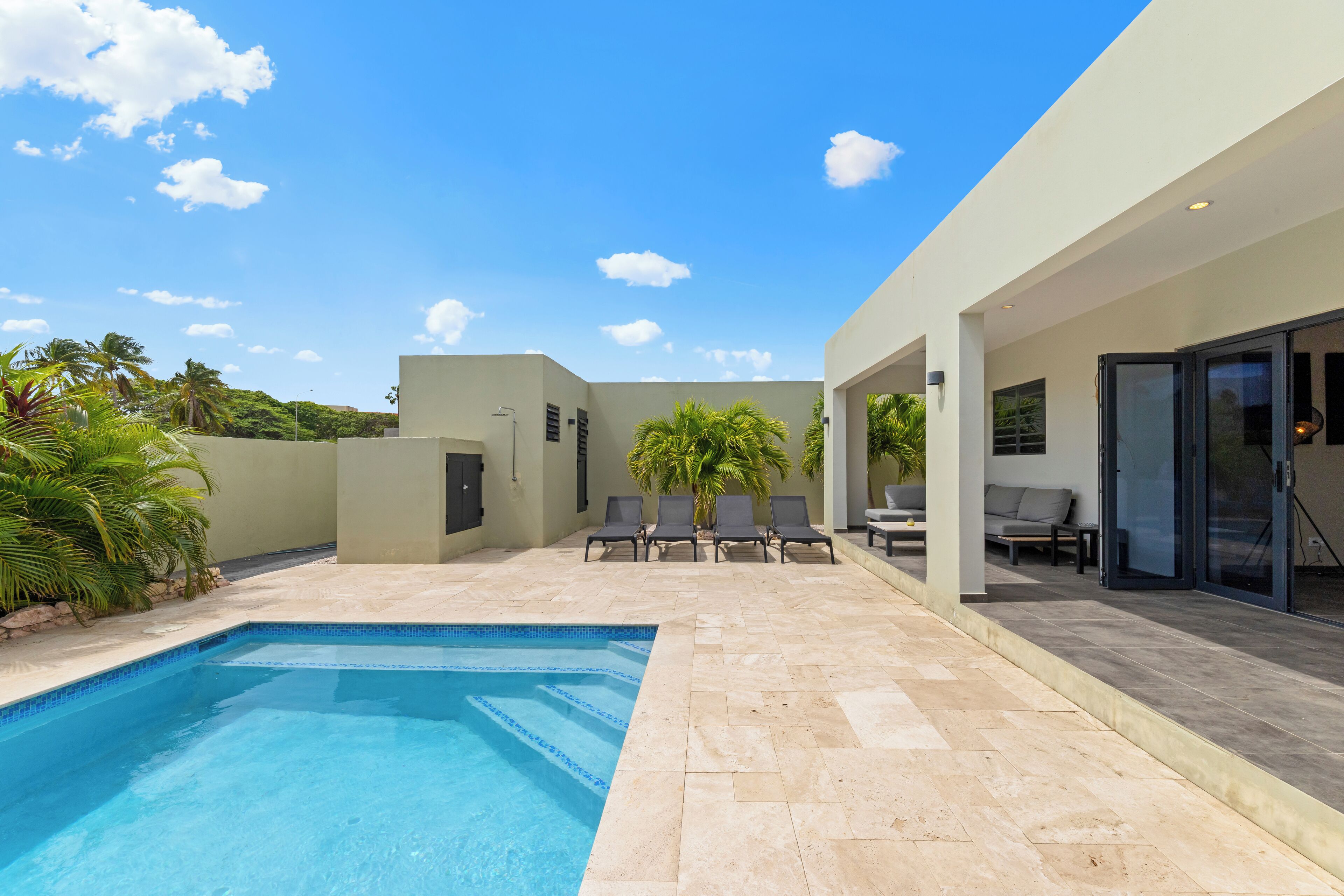 A modern outdoor pool area with a clear blue pool, lounge chairs, and a covered seating area.