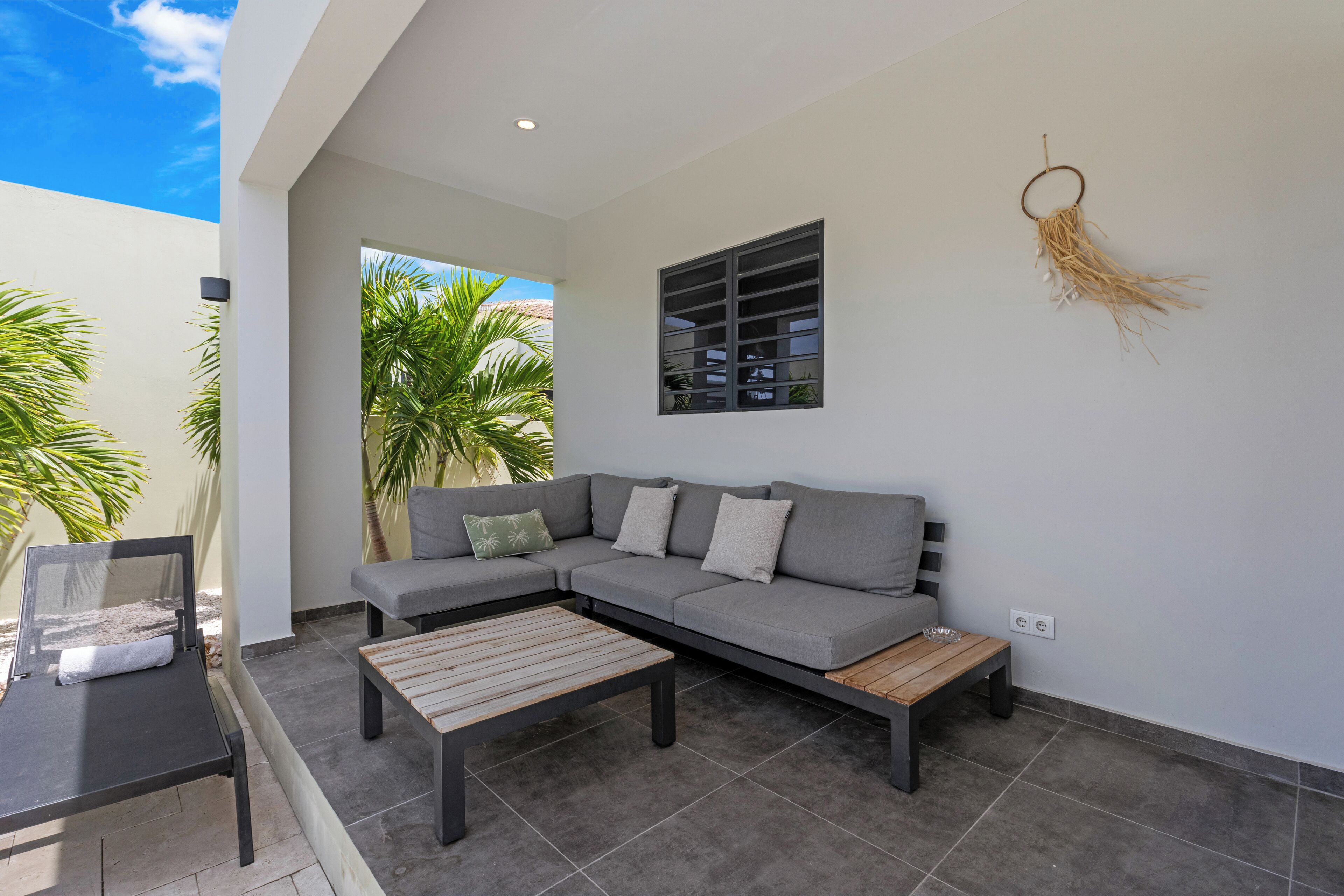 A modern outdoor living area with a grey sectional sofa, a wooden coffee table, and a small side table.