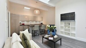 A modern living room with a sofa, coffee table, and a dining area with chairs and a kitchen in the background.