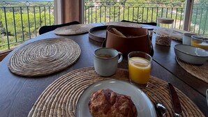Ett frukostbord med en croissant, en kopp och ett glas apelsinjuice, med utsikt över ett vackert landskap med en balkong och ett bergigt område.