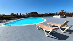 Une piscine avec un revêtement de sol en carrelage et des chaises longues.