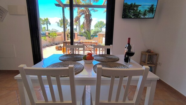 Un coin repas avec une table dressée pour deux personnes, une bouteille de vin et un saladier de fruits.