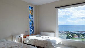 A bedroom with two beds, a large window with a view of the sea, and a colorful abstract painting on the wall. - Villa Paraíso in Mojácar with pool for 14 guests – 7 bedrooms – 3.5 bathrooms (Mojácar)