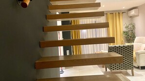 Una escalera de madera con barandilla que conduce a una habitación con una silla estampada y un sofá blanco.