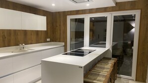 Una cocina moderna con una isla central, muebles blancos y un ventanal que da a un comedor.