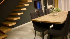 Un comedor moderno con una mesa y sillas de madera, una escalera con peldaños de madera y una planta en maceta sobre la mesa.
