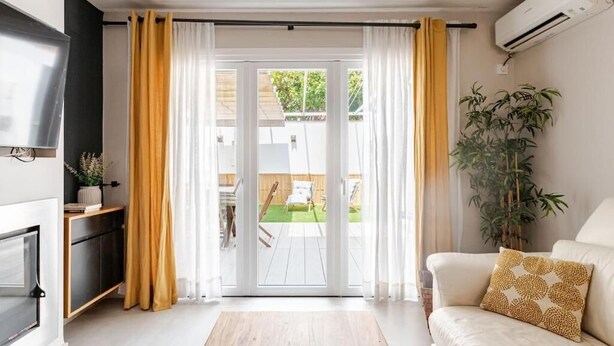 Una sala de estar con sofá, televisor, planta y puerta corrediza de vidrio al exterior.