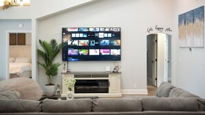 A living room with a flat-screen TV mounted on the wall, a fireplace, a potted plant, and a sofa. - DFW Spacious Cozy Modern Villa (Grand Prairie)