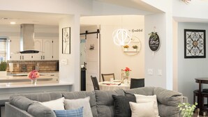 A modern living room with a grey sectional sofa, a glass coffee table, and a dining area in the background. - DFW Spacious Cozy Modern Villa (Grand Prairie)