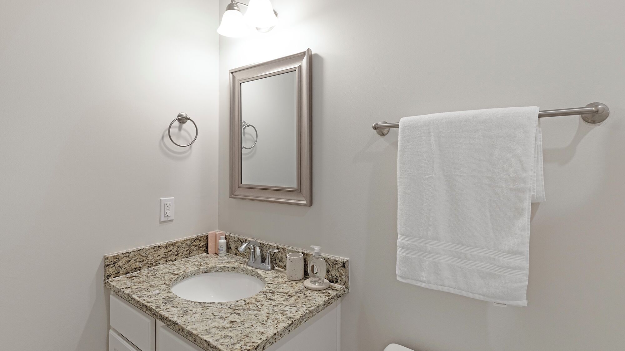 A bathroom with a granite countertop sink, a mirror, a towel rack, and a light fixture.