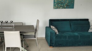 A dining area with a table and chairs, a green sofa with patterned cushions, and a wall-mounted artwork. - Quiet house with garden Pets welcome (Sakiet Ezzit)