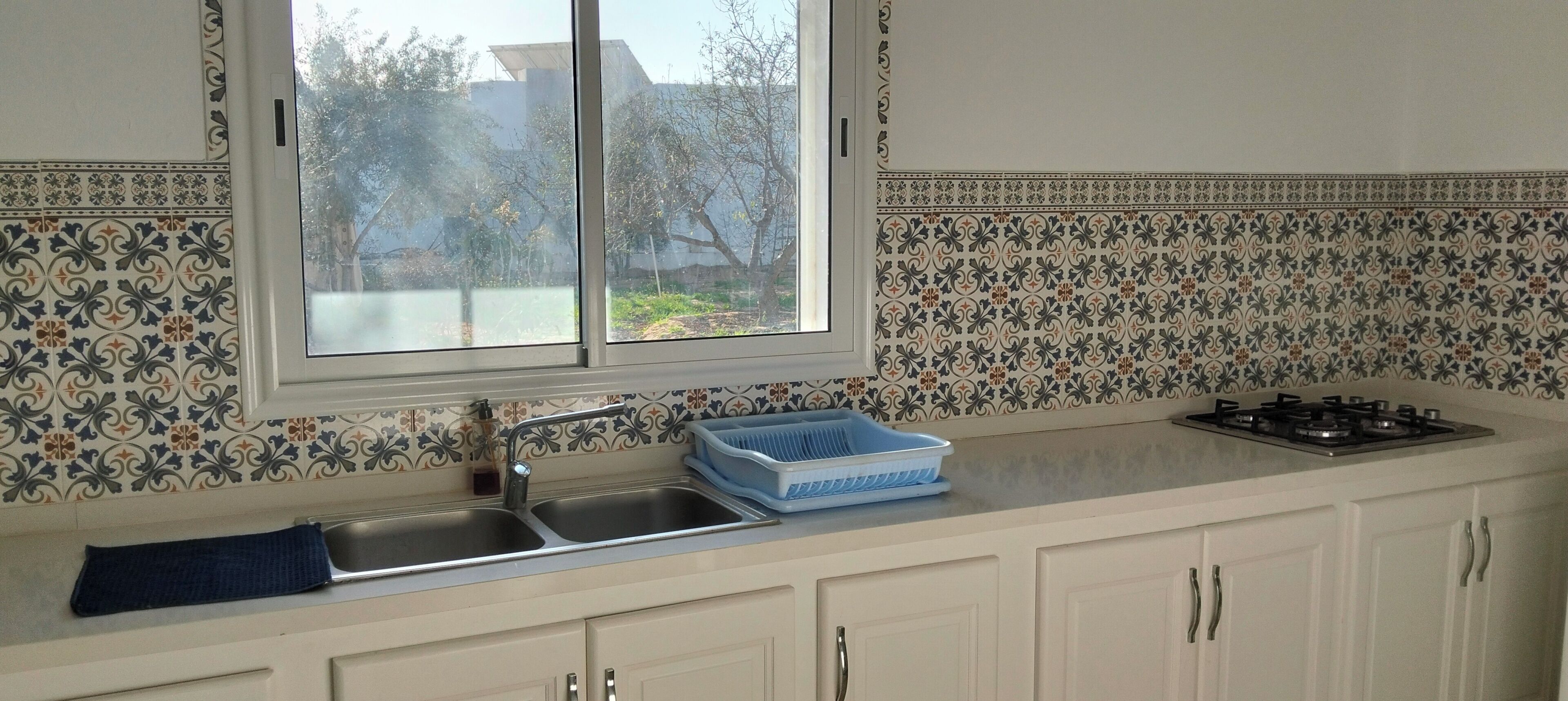 A kitchen with a window, sink, stove, and patterned backsplash.