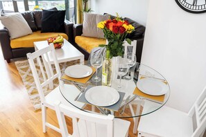 Uma área de refeições com mesa de vidro, cadeiras brancas e um vaso de flores.