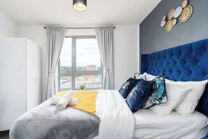 Quarto de hotel com uma cama grande, vista da cidade pela janela e cabeceira azul.