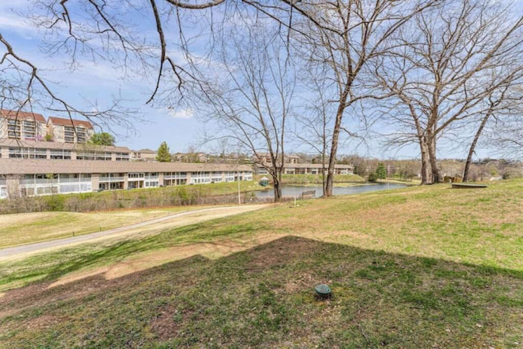A grassy area with a path leading to a building with multiple windows and a pond in the background.