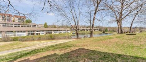 A grassy area with a path leading to a building with multiple windows and a pond in the background.