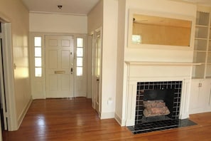 A hallway with wooden flooring, a white door, and a fireplace with a mantel.