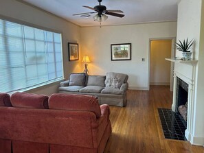 Ein Wohnzimmer mit Sofa, Kamin, Deckenventilator und einem Fenster mit Jalousien.