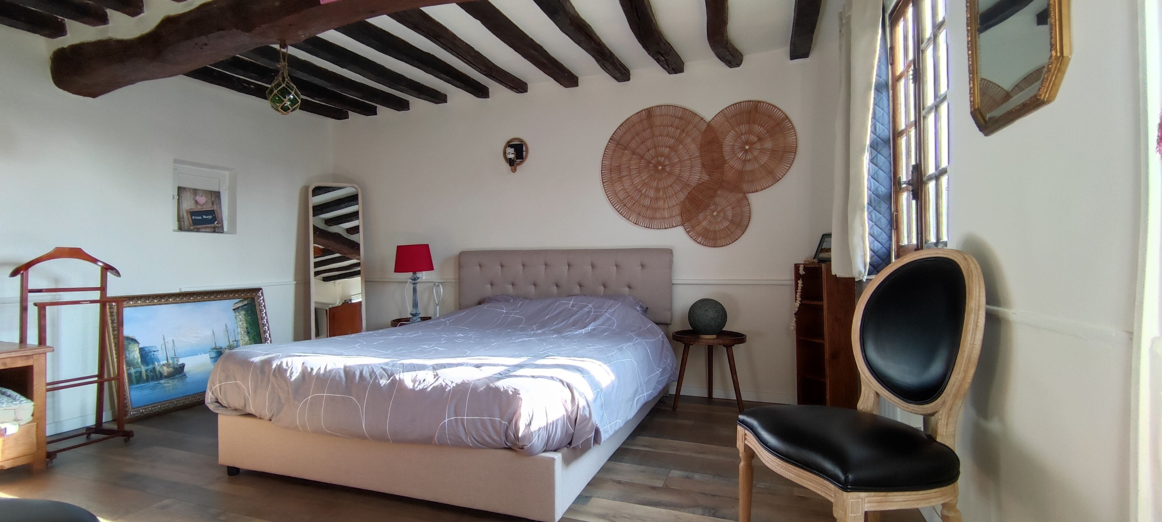 Une chambre à coucher avec un grand lit, une chaise, un fauteuil en bois, une lampe, un miroir et un élément de décoration murale.
