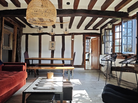 A room with exposed wooden beams, a woven light fixture, a wooden bench, a dining table, and a view through a window.. Battlefield longhouse