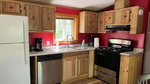 A compact kitchen with wooden cabinets, a white refrigerator, a dishwasher, a stove, and a sink. - White Pines B&B LLC (Blackduck)