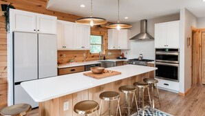 A modern kitchen with white cabinets, a large island with stools, stainless steel appliances, and wooden ceiling beams.