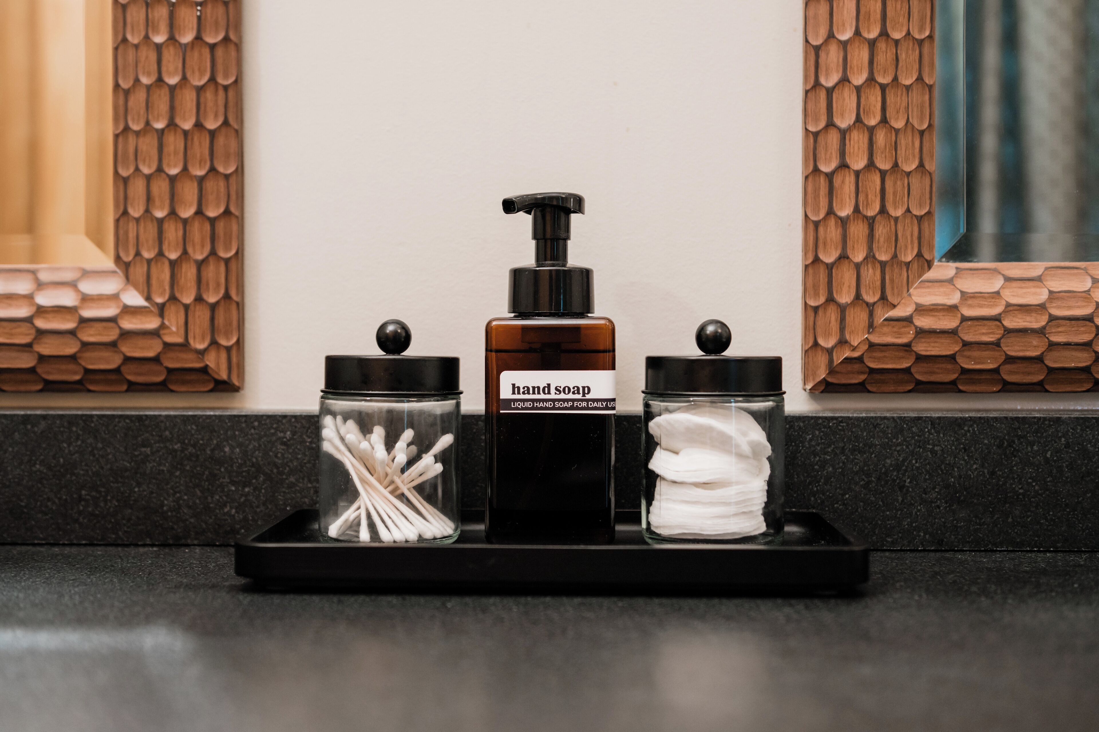 A bathroom vanity with a soap dispenser, a container of cotton swabs, and a jar of hand soap.