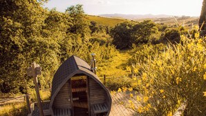 A wooden cabin with a curved roof, situated on a wooden deck surrounded by lush greenery and yellow flowers. - Boutique eco Agriturismo nestled among ancient olive trees and stunning Tuscan hills (Santa Luce)