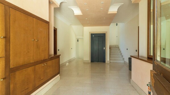 Un hall d’entrée spacieux, avec une armoire en bois, une porte sombre au fond et un escalier menant à l’étage.