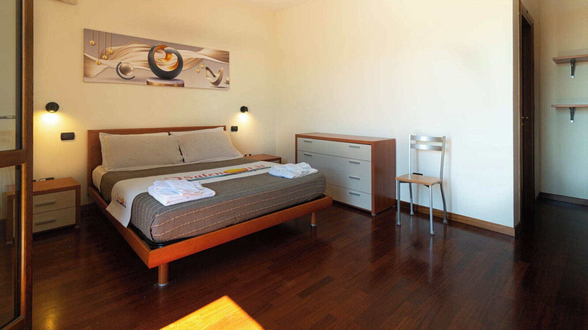 A neatly arranged bedroom with a bed, bedside tables, a desk, and a chair.