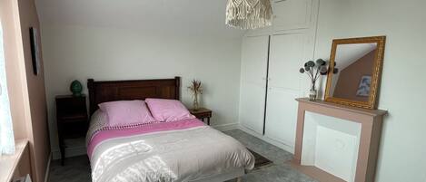 A bedroom with a bed, bedside tables, a dresser, a mirror, and a hanging light fixture.