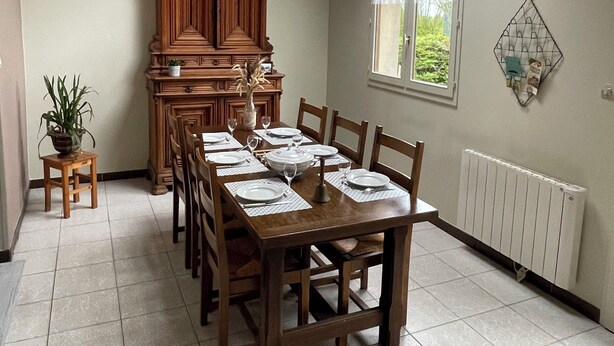 A dining room with a high ceiling, a skylight, a wooden cabinet, a dining table set for six, and a radiator on the wall. - A unique stay in an old railway station, in the heart of the Cotentin sea & countryside. (Saint-Georges-de-la-Rivière)