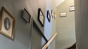 A staircase with wooden steps and a wooden handrail, leading up to a landing with a light green wall and several framed pictures. - A unique stay in an old railway station, in the heart of the Cotentin sea & countryside. (Saint-Georges-de-la-Rivière)