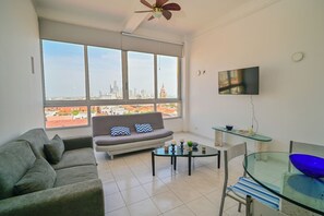 A modern living room with a sofa, a glass coffee table, a TV, and a large window with a city view. - Charming 1-bedroom apartment with AC, WiFi in beautiful Cartagena de Indias (Cartagena de Indias)