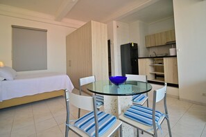 Un dormitorio con una cama, una mesa de vidrio con sillas, un tazón azul y una zona de cocina con armarios de madera.