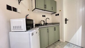 Une cuisine de taille réduite, avec un réfrigérateur blanc, un four à micro-ondes, une bouilloire et des placards verts.