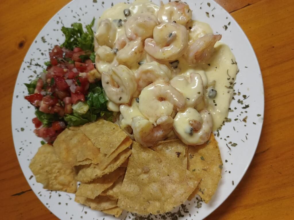 Een bord met garnalen in saus, een kleine salade en tortilla chips.