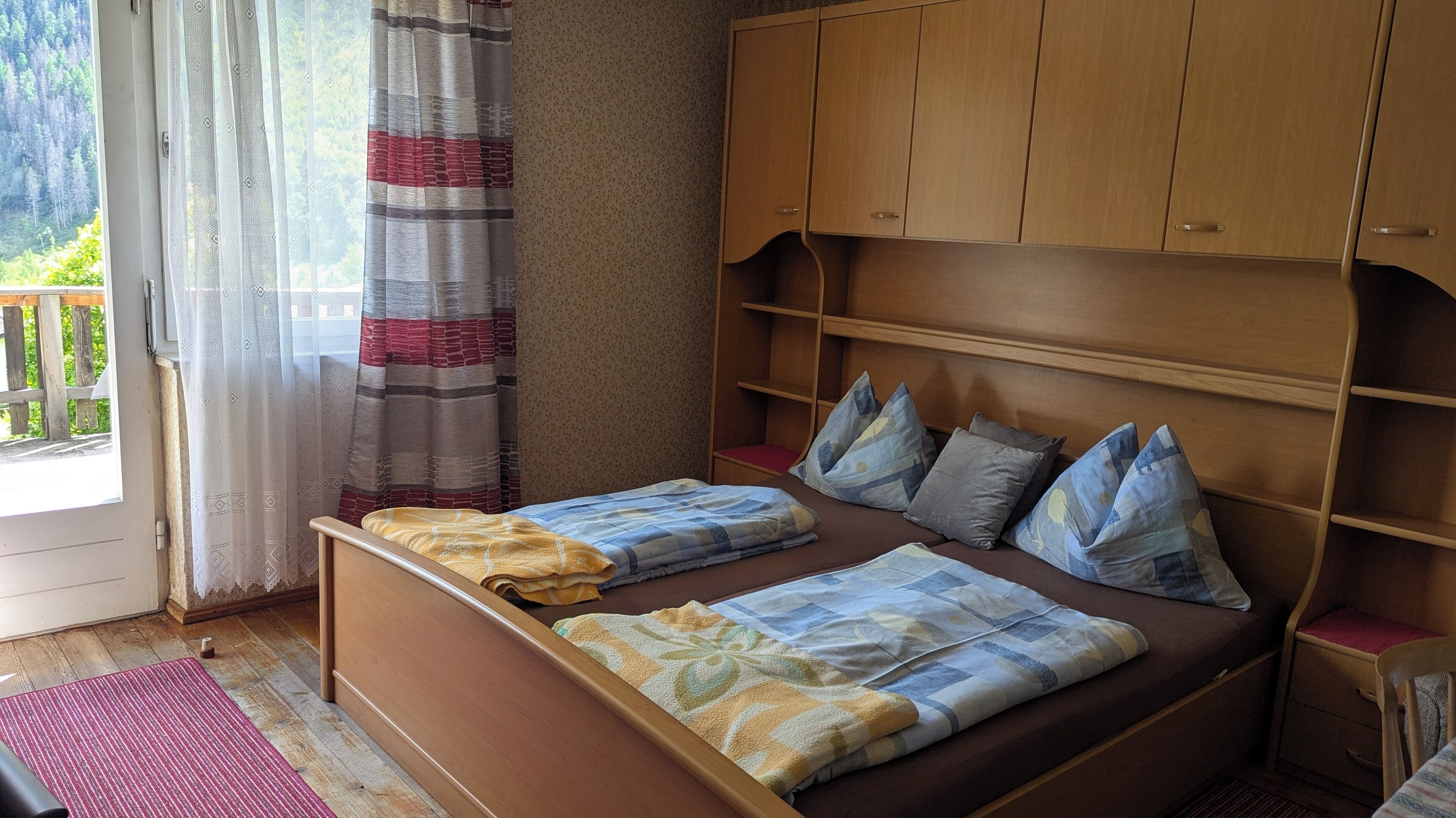 Un dormitorio con cama de madera, cortina a rayas rojas y blancas, y un armario de madera.
