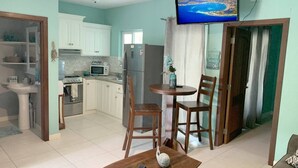 Amplia sala de estar con cocina, mesa de comedor y televisor instalado en la pared.
