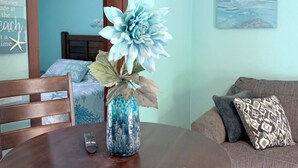 Un comedor con una mesa de madera, un florero con arreglo floral, un control remoto y un sofá con almohadones estampados.