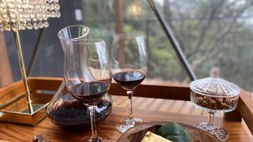A wooden tray with two wine glasses, a pitcher, a cheese plate, and a coffee container.