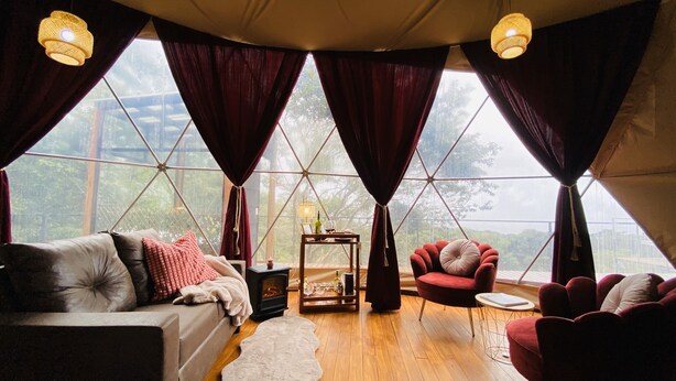 A cozy room with a sofa, armchairs, and a small table with drinks. Large windows offer a view of greenery outside. - Monteverde Rainforest Domes (Monteverde)