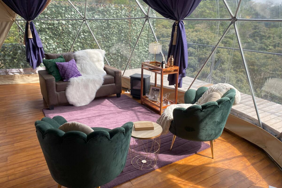 Habitación acogedora con sofá, dos sillones y una mesita, con un ventanal que ofrece vistas a zonas verdes.