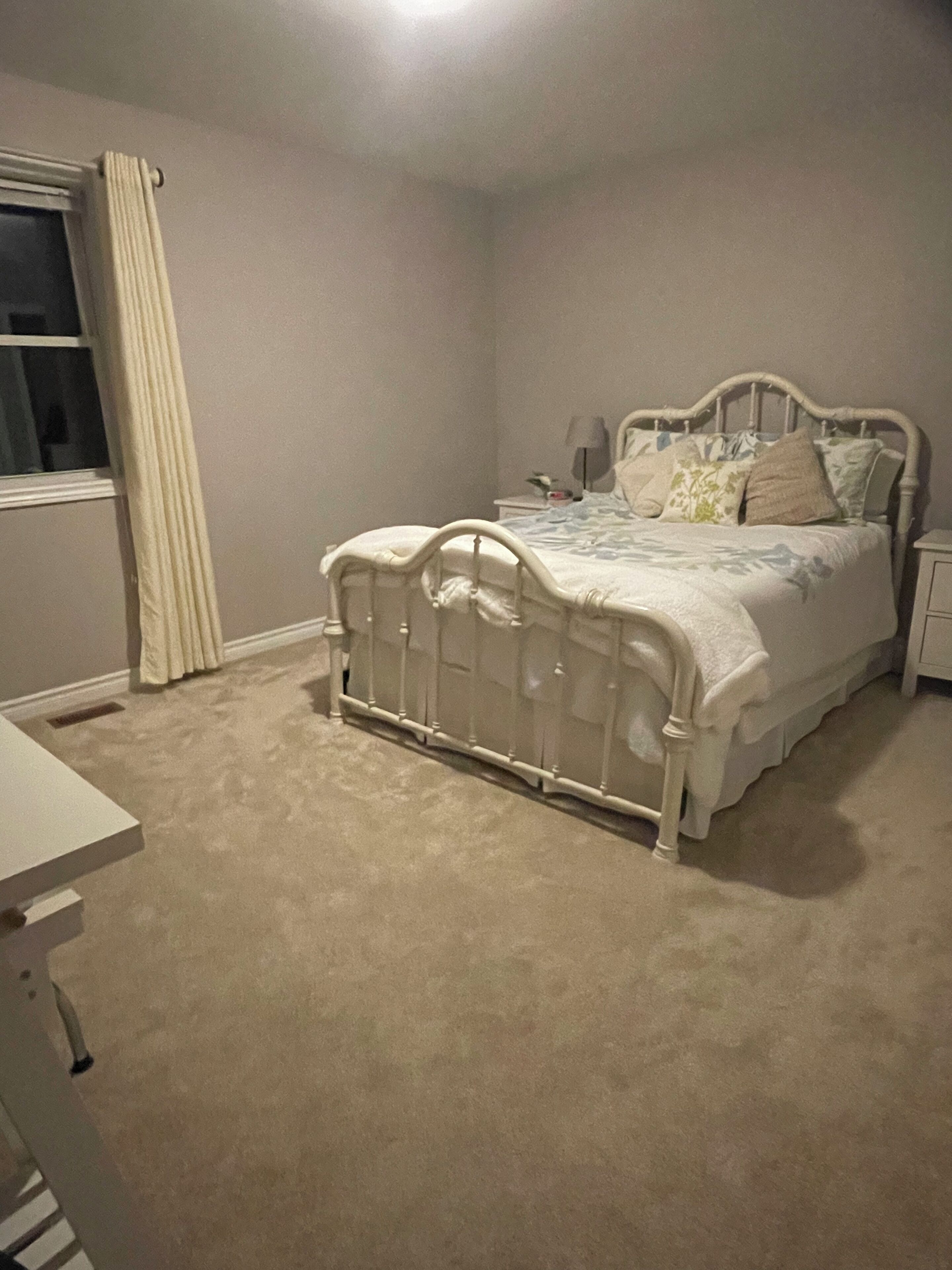 A bedroom with a bed, nightstand, and a window with curtains.
