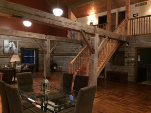 Una habitación amplia con una mesa de vidrio, sillas de madera, una chimenea y una escalera de madera.