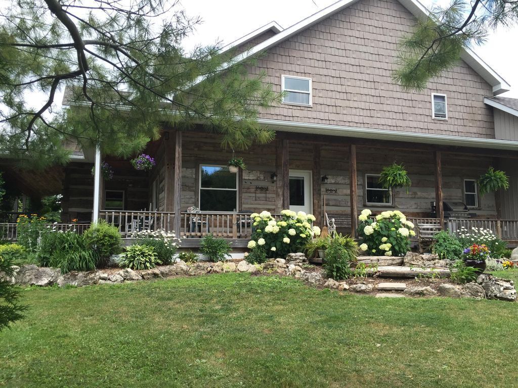 A two-story log cabin with a porch, surrounded by a well-maintained garden with various plants and flowers.
